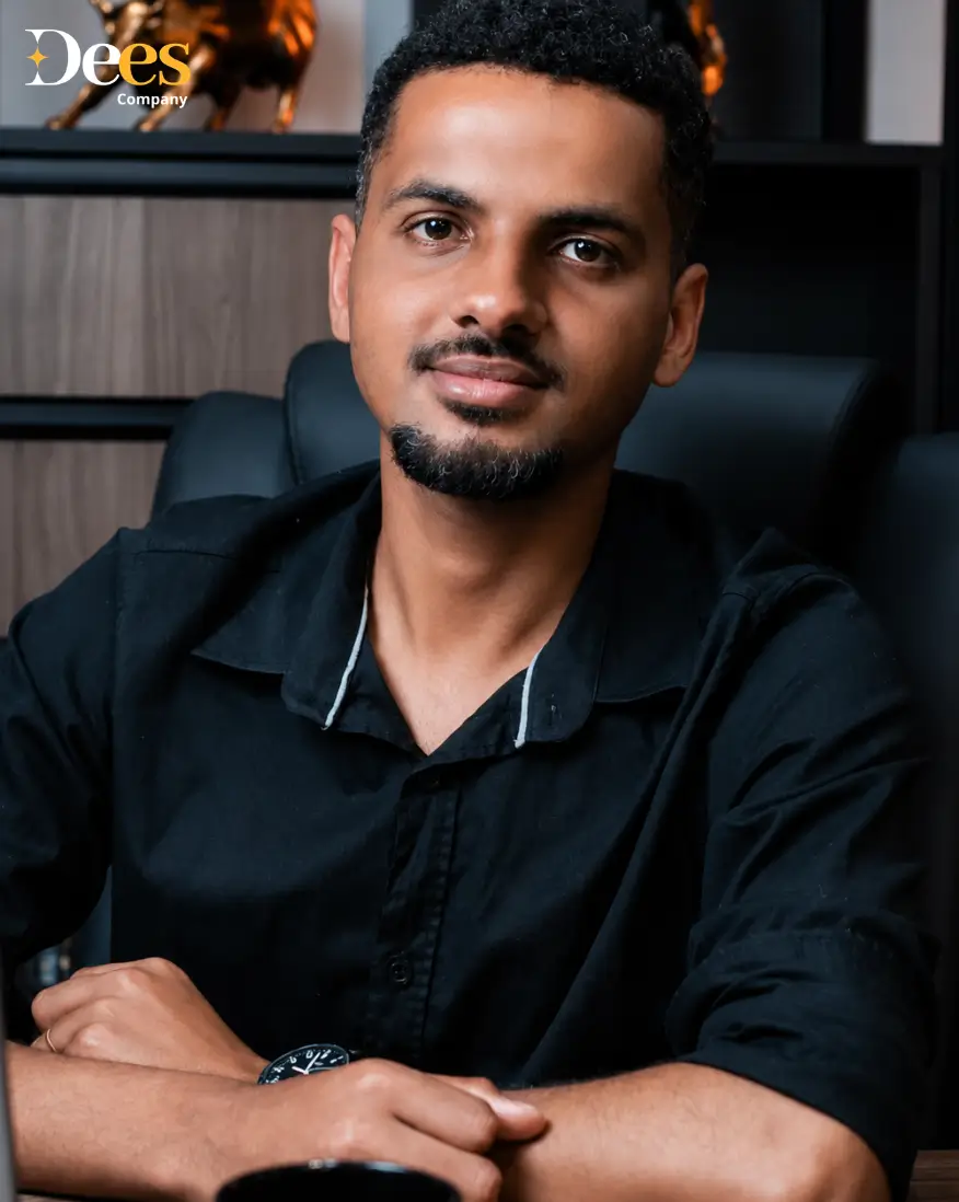 Marcos Oliveira, especialista em Proteção Patrimonial na Dees Company. Homem de camisa preta em ambiente de escritório com o logo da empresa ao fundo.